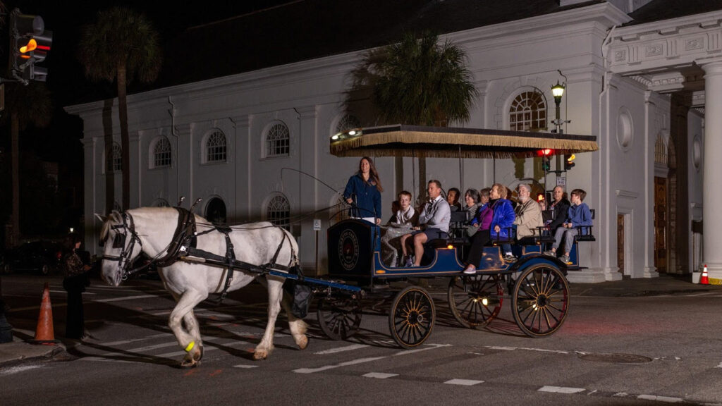 A horse-drawn carriage in front of the red barn of Palmetto Carriage Works, ready for a historic bars tour.